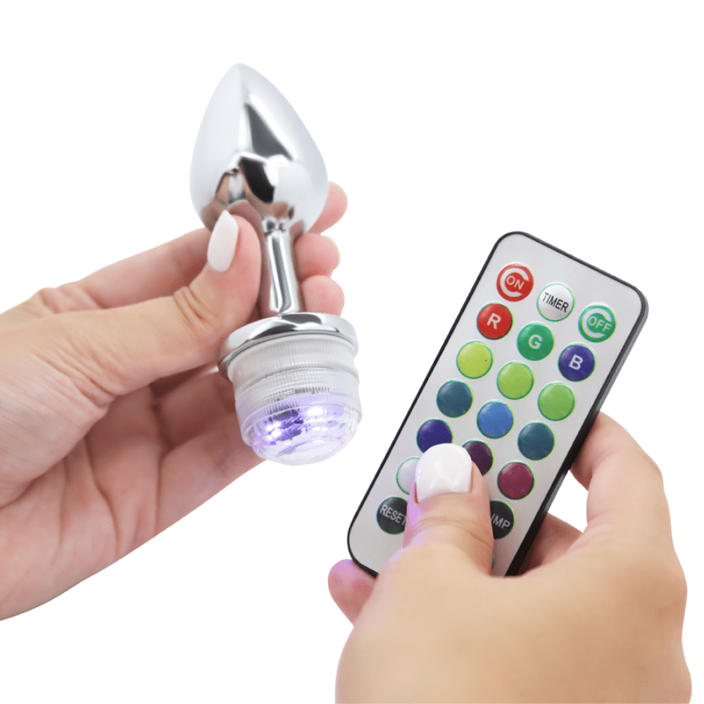 Image of a hand holding the anal plug and the remote, with the base of the anal plug purple.