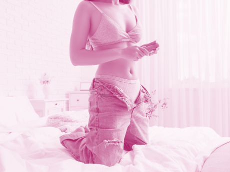 WOMAN WITH UNBUTTONED JEANS HOLDING VIBRATOR IN BED