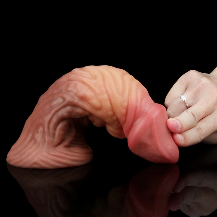 fingers pushing down penis tip of Dual-Density Fantasy Cock layered Platinum Silicone Plug from Lovetoy to show flexibility 