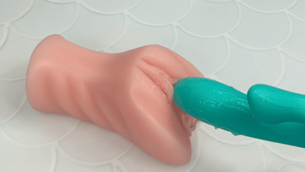 GIF of teal dual action vibrator vibrating on beige masturbator