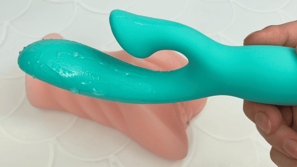 GIF of teal dual action vibrator turned on in front of beige masturbator