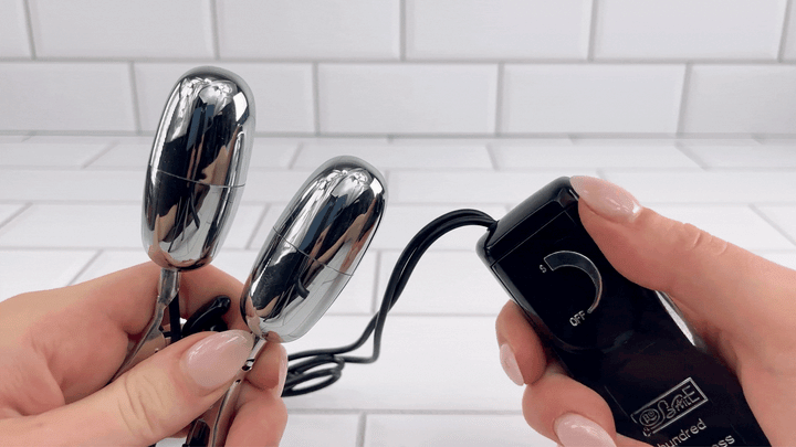 GIF of womans hands turning on Vibrating Power Bullet Nipple Clamps with remote control 
