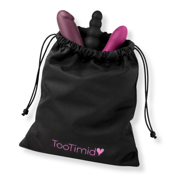 A black drawstring pouch with the TooTimid logo printed in pink on the front, containing two intimate massagers in matte purple and black, set against a plain white background.