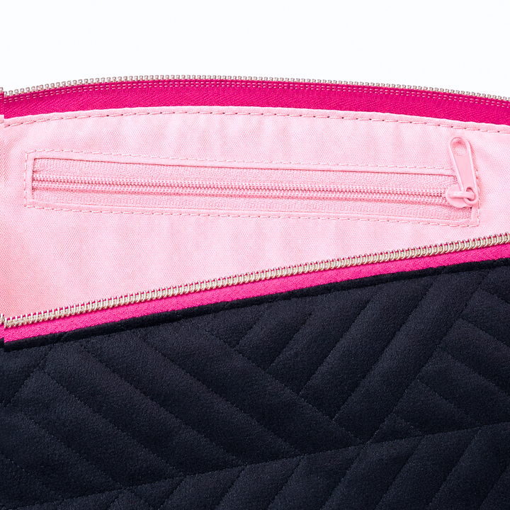 Close-up of a quilted bag showing a black chevron-quilted exterior, a bright pink inner pocket, and a hot pink zipper trim with a silver zipper.