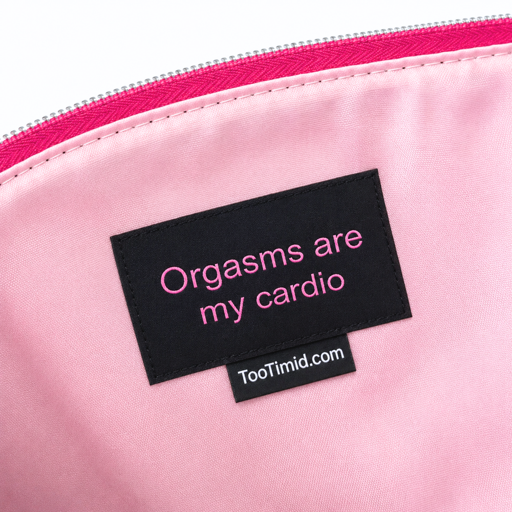 Close-up of a pink zippered pouch or bag interior with a black label reading 'Orgasms are my cardio' and 'TooTimid.com'.