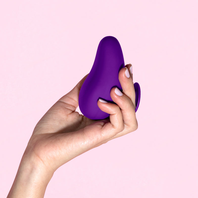 Blush Novelties purple palm vibrator being held by a hand with light purple nail polish with a light purple background